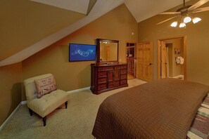 A bedroom with a sloped ceiling, a bed, a dresser, a chair, and a large mirror.