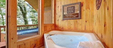 A wooden cabin bathroom with a hot tub, a wooden deck outside, and a framed quote on the wall.
