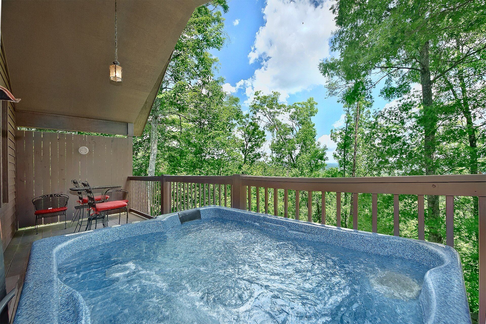 Un bain à remous sur une terrasse en bois, avec vue sur les arbres et un ciel dégagé.