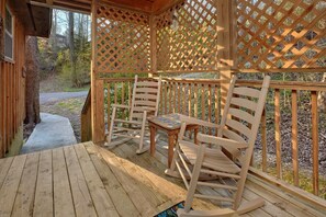 Eine Holzterrasse mit Gitterdach, zwei Schaukelstühle und ein kleiner Tisch.