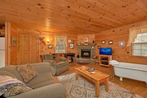 Ein gemütliches Blockhaus-Interieur mit Kamin, Fernseher, Sofa und Badewanne.