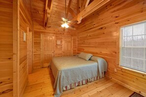 Ein Zimmer in einer Holzhütte mit einem Bett, einem Deckenventilator und einem Fenster mit Jalousien.