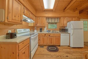 Une cuisine rustique aménagée dans une cabane en bois, comprenant un poêle, un four à micro-ondes, un réfrigérateur et des placards en bois.