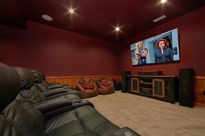 A home theater room with a large screen, leather recliner, and a wooden cabinet. - Hideaway Dreams | Theater, Smoky Mtn Views, Hot Tub, Game Room, Sleeps 12 + Free Attraction Tickets (Wears Valley)