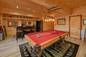 Ein Holzinterieur mit Poolbillard, Stühlen, einer Bar und einem Kamin.