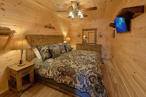 A cozy wooden room with a bed, a nightstand, a dresser, a ceiling fan, and a television. - Hideaway Dreams | Theater, Smoky Mtn Views, Hot Tub, Game Room, Sleeps 12 + Free Attraction Tickets (Wears Valley)