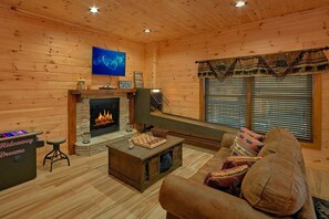 A cozy log cabin interior with a fireplace, a television mounted above it, and a comfortable seating area with a couch and a coffee table. - Hideaway Dreams | Theater, Smoky Mtn Views, Hot Tub, Game Room, Sleeps 12 + Free Attraction Tickets (Wears Valley)