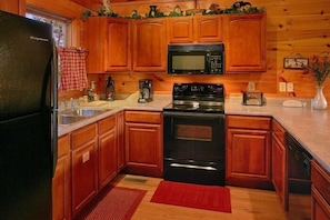A kitchen with wooden cabinets, a black refrigerator, a microwave, a stove, and a sink. - I Don't Want 2 Leave Cabin Rental (Wears Valley)