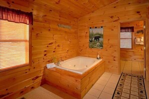 A wooden cabin interior with a large wooden bathtub, a window with blinds, and a picture on the wall. - I Don't Want 2 Leave | Mtn Views, Hot Tub, Fireplace + Free Attraction Tickets (Wears Valley)