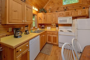 A wooden cabin kitchen with a stove, microwave, sink, and a white chair. - Jasmine's Retreat | Hot Tub, Game Room, Fireplace + Free Attraction Tickets (Wears Valley)