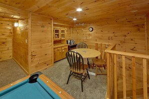 A wooden cabin interior with a pool table, a dining table with chairs, a kitchen area, and a clock on the wall. - Jasmine's Retreat | Hot Tub, Game Room, Fireplace + Free Attraction Tickets (Wears Valley)