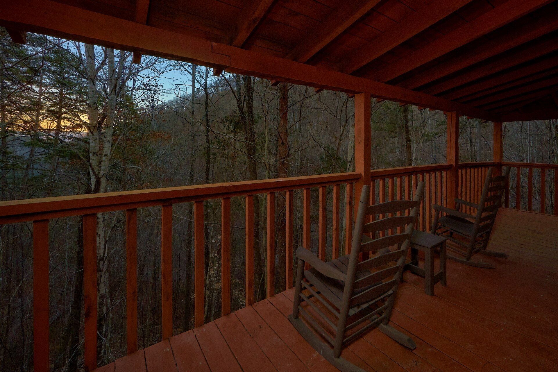 A wooden deck with a railing, overlooking a forested area.