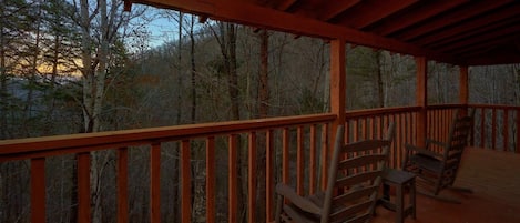A wooden deck with a railing, overlooking a forested area.