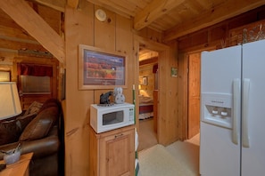 A wooden interior with a brown leather sofa, a white microwave, and a refrigerator. - Just Barely Making It | Hot Tub, Fireplace + Free Attraction Tickets (Wears Valley)