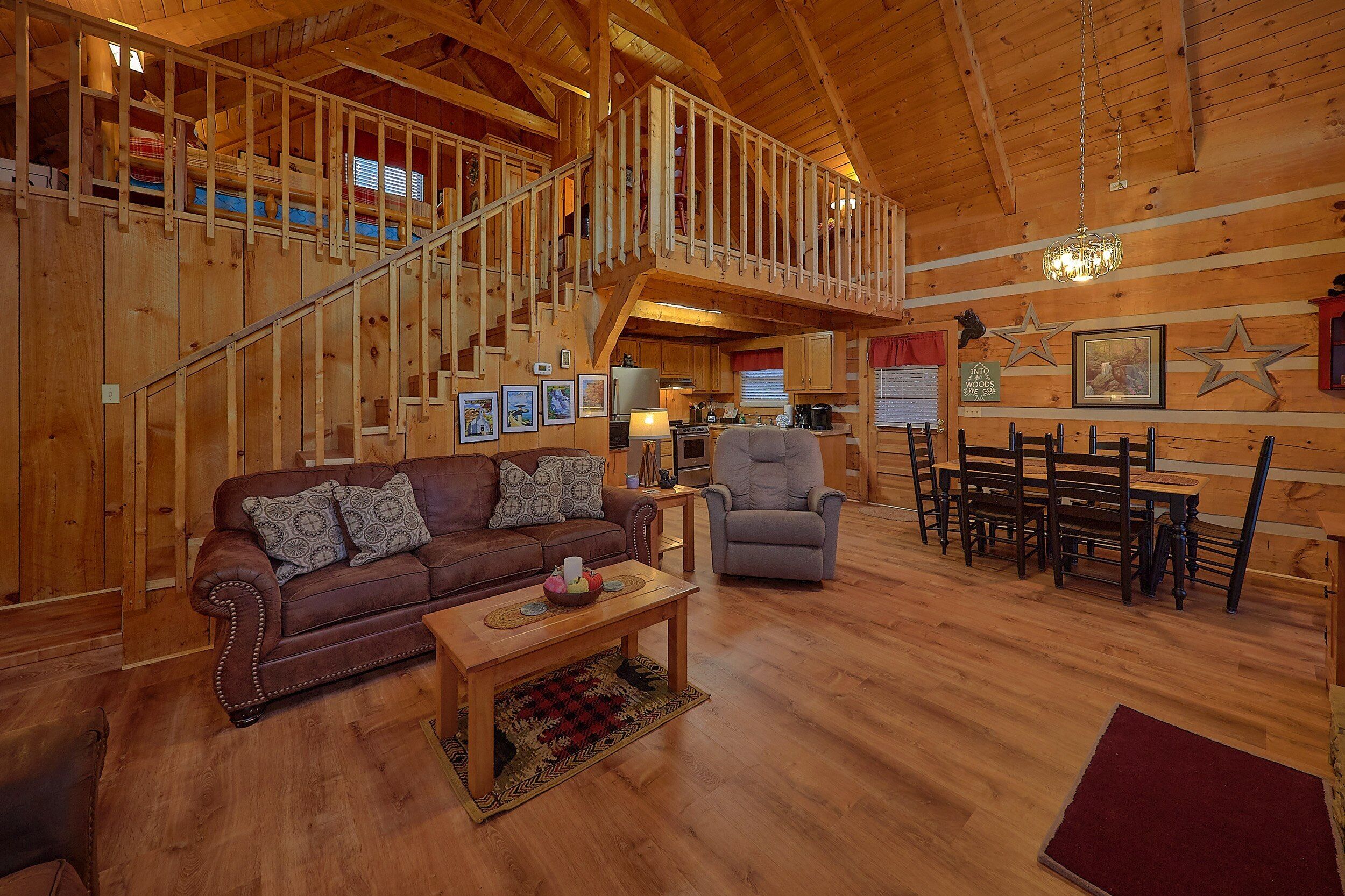 A wooden interior with a staircase, a sofa, a dining table with chairs, and a kitchen area.