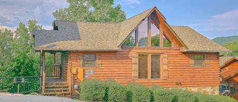 A log cabin with a steeply pitched roof, large windows, and a porch.