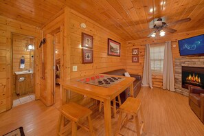 A cozy cabin interior with wooden walls, a dining table with chairs, a sofa, a fireplace, and a television. - Knockin On Heaven's Door | Hot Tub, Arcade, Sleeps 12, King Suites + Free Attraction Tickets (Sevierville)
