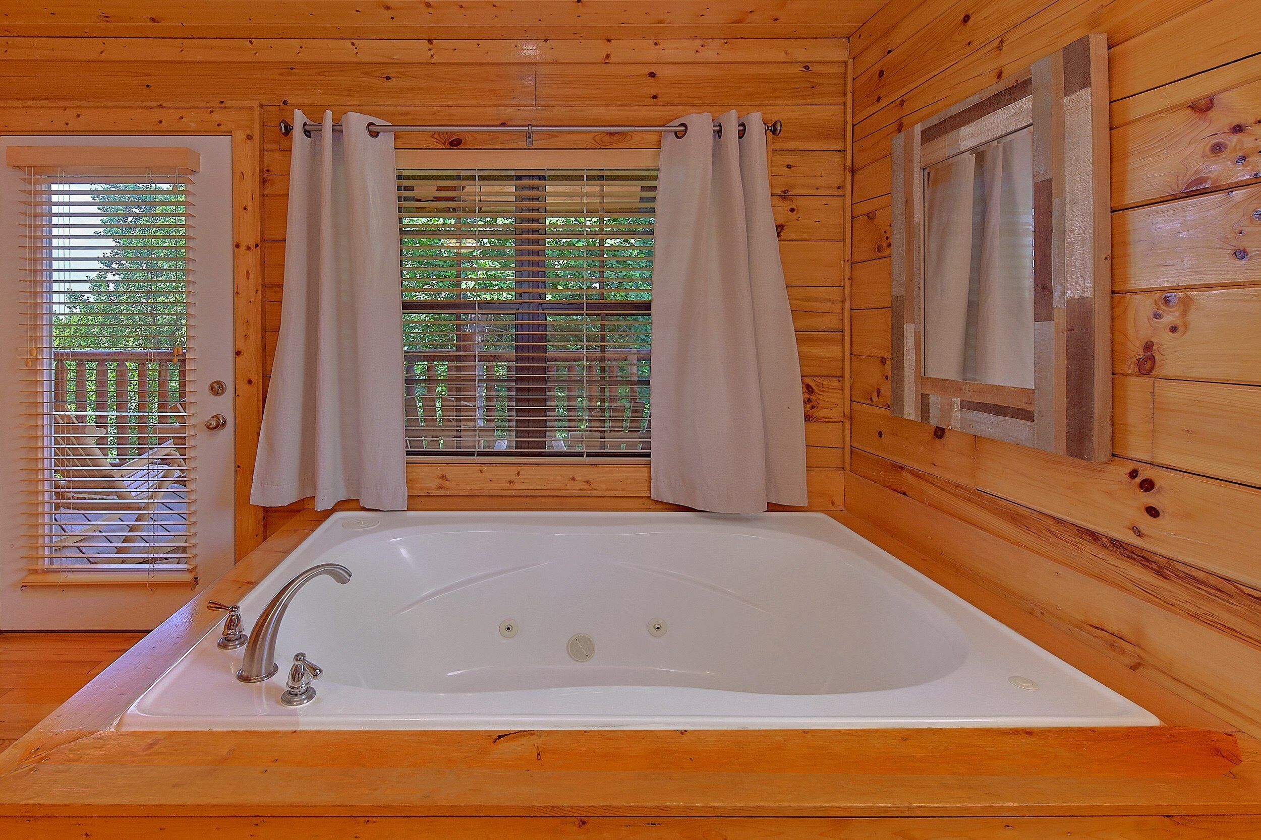L’intérieur d’un chalet en bois, avec une grande baignoire, des murs en bois et une fenêtre équipée de stores.