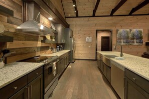 A modern kitchen with wooden paneling, stainless steel appliances, and granite countertops. - LeConte Views | Theater, Smoky Mtn Views, Hot Tub, Game Room, Sleeps 14 + Free Attraction Tickets (Gatlinburg)