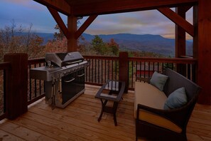 Eine Holzterrasse mit Grill, Tisch und einer Sitzecke mit Kissen.