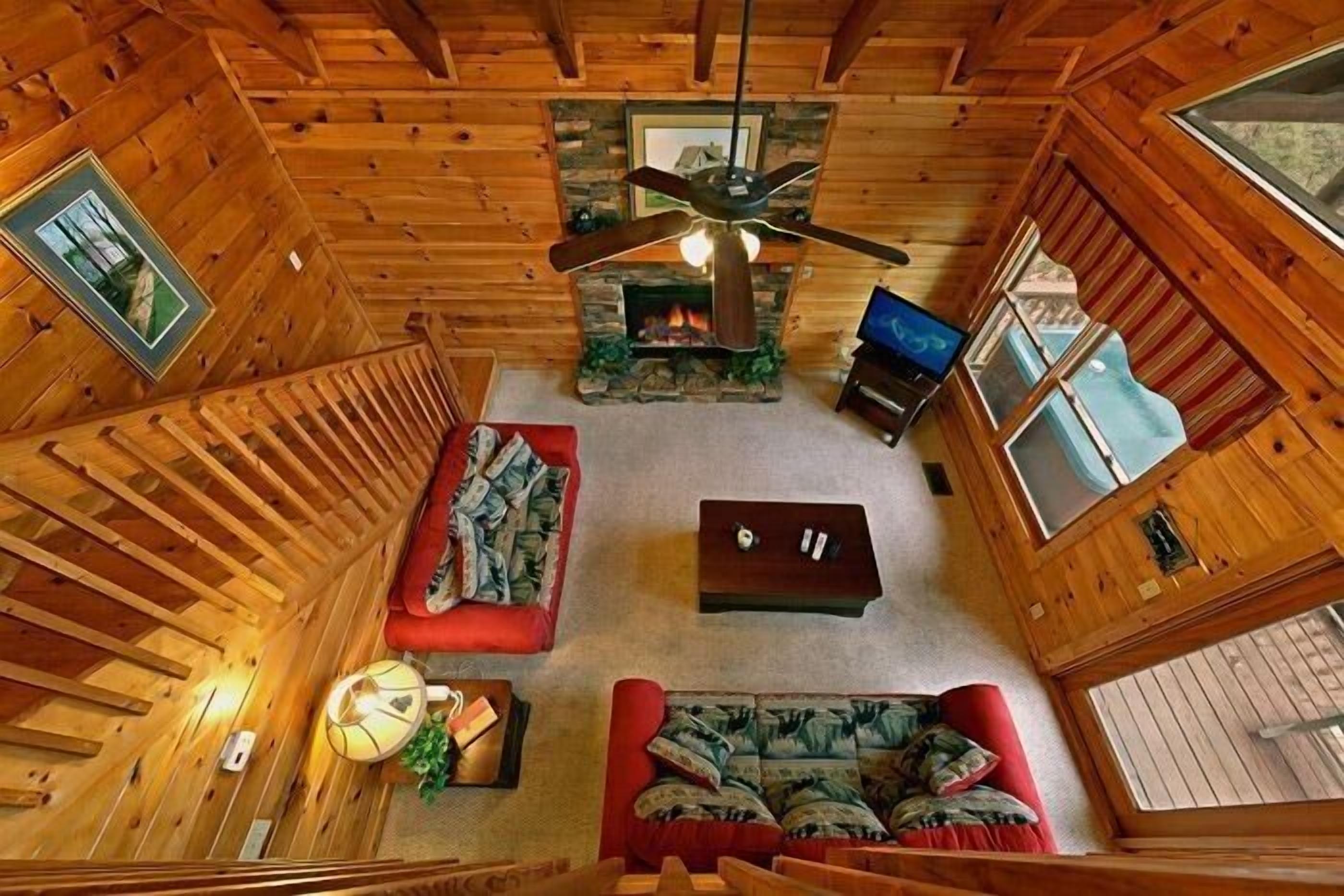 A cabin interior with a fireplace, a ceiling fan, a television, and a cozy seating area.
