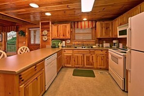 A kitchen with wooden cabinets, a countertop, a sink, and a refrigerator. - Little Cove Hideaway | Hot Tub, Game Room, Fireplace + Free Attraction Tickets (Wears Valley)