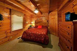 A wooden cabin bedroom with a bed, dresser, and a television. - Little Cove Hideaway | Hot Tub, Game Room, Fireplace + Free Attraction Tickets (Wears Valley)