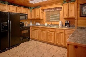 A kitchen with wooden cabinets, a black refrigerator, a stove, and a microwave. - Lookin Up | Hot Tub, Game Room, Pigeon Forge, Resort Pool, Fireplace + Free Attraction Tickets (Pigeon Forge)
