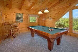 A wooden interior with a pool table, chairs, and a window with a view. - Lookin Up | Hot Tub, Game Room, Pigeon Forge, Resort Pool, Fireplace + Free Attraction Tickets (Pigeon Forge)