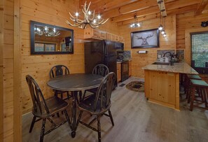 A wooden interior with a dining table and chairs, a kitchen area, and a chandelier. - Lovers Paradise | Hot Tub, Game Room, Pigeon Forge, Resort Pool, Fireplace + Free Attraction Tickets (Pigeon Forge)