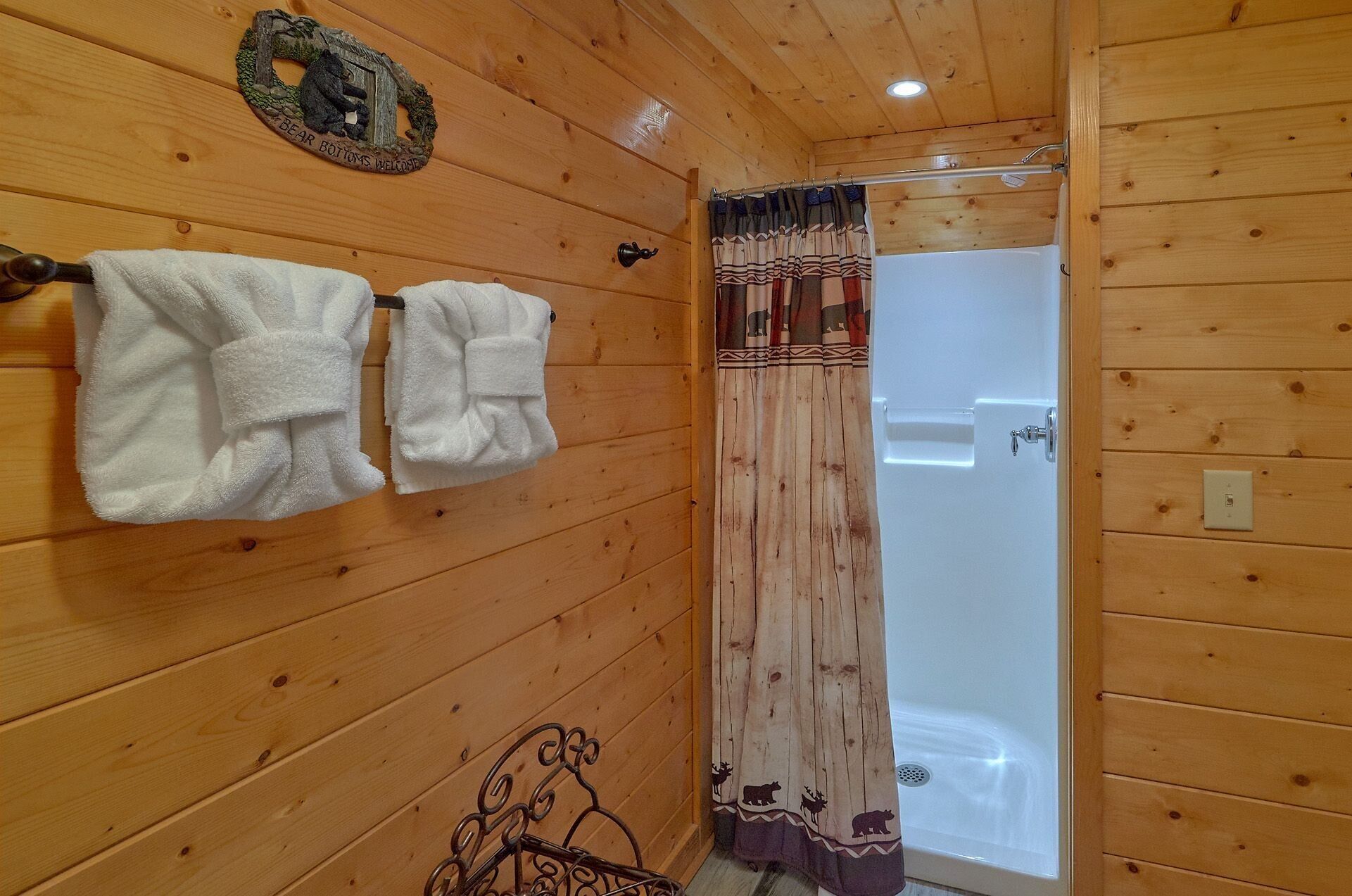 Casa de madeira com banheiro, com duas toalhas penduradas em um suporte, cortina de chuveiro com estampas de animais e uma parede de madeira com decoração de urso.