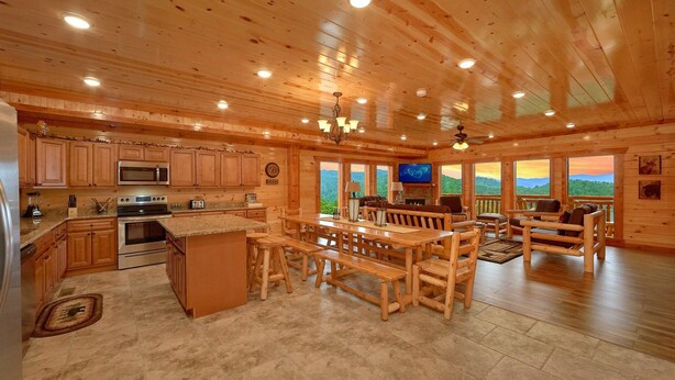 A spacious log cabin interior with a kitchen, dining area, and a large window overlooking a mountainous landscape.