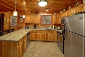 A cabin-style kitchen with wooden cabinets, a granite countertop, a stainless steel refrigerator, and a built-in oven. - Major Oaks | Theater, Hot Tub, Game Room, Sleeps 12, King Suites + Free Attraction Tickets (Pigeon Forge)