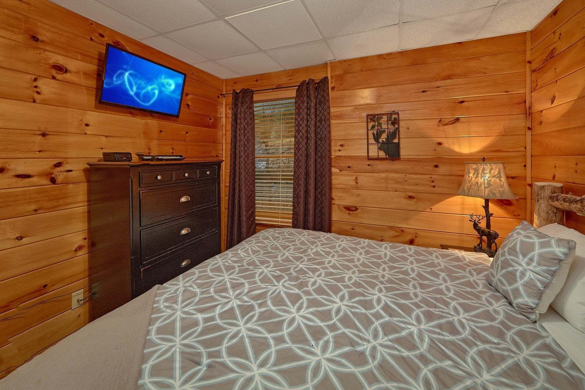 Una camera in una baita di legno con un letto, una cassettiera, un televisore e una lampada.