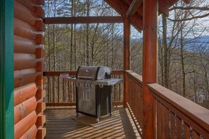 A wooden deck with a grill, surrounded by trees and a mountainous backdrop. - Major Oaks | Theater, Hot Tub, Game Room, Sleeps 12, King Suites + Free Attraction Tickets (Pigeon Forge)