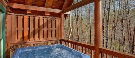 Ein Whirlpool auf einer Holzterrasse mit Blick auf einen Wald.