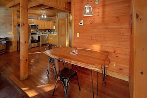 A wooden interior with a dining table and chairs, a kitchen area, and a wooden wall with a light fixture. - Merry Weather | Mtn Views, Hot Tub, Fireplace + Free Attraction Tickets (Sevierville)