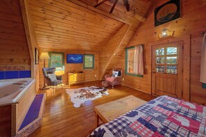 A cabin interior with a wooden ceiling, a television, a fireplace, a sofa, a wooden table, and a quilted bedspread. - Merry Weather | Mtn Views, Hot Tub, Fireplace + Free Attraction Tickets (Sevierville)
