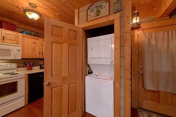 A wooden interior with a kitchen area including a microwave, stove, and washing machine. - Merry Weather | Mtn Views, Hot Tub, Fireplace + Free Attraction Tickets (Sevierville)