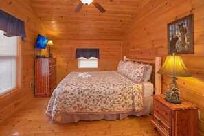 A wooden cabin bedroom with a bed, dresser, lamp, and a ceiling fan. - Moonshine Inn | Hot Tub, Game Room, Gatlinburg, Resort Pool, Fireplace + Free Attraction Tickets (Gatlinburg)