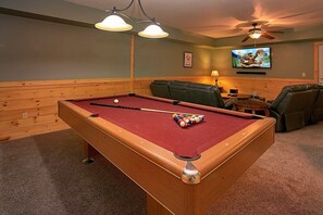 A pool table with balls, a television, and leather chairs in a room with wooden paneling. - Moonshine Inn | Hot Tub, Game Room, Gatlinburg, Resort Pool, Fireplace + Free Attraction Tickets (Gatlinburg)