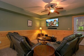 A room with a ceiling fan, a television mounted on the wall, a framed picture, and a window with curtains. - Moonshine Inn | Hot Tub, Game Room, Gatlinburg, Resort Pool, Fireplace + Free Attraction Tickets (Gatlinburg)