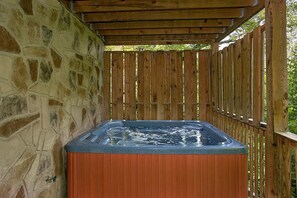 A hot tub in a covered outdoor area with stone walls and wooden fencing. - Moonshine Inn | Hot Tub, Game Room, Gatlinburg, Resort Pool, Fireplace + Free Attraction Tickets (Gatlinburg)