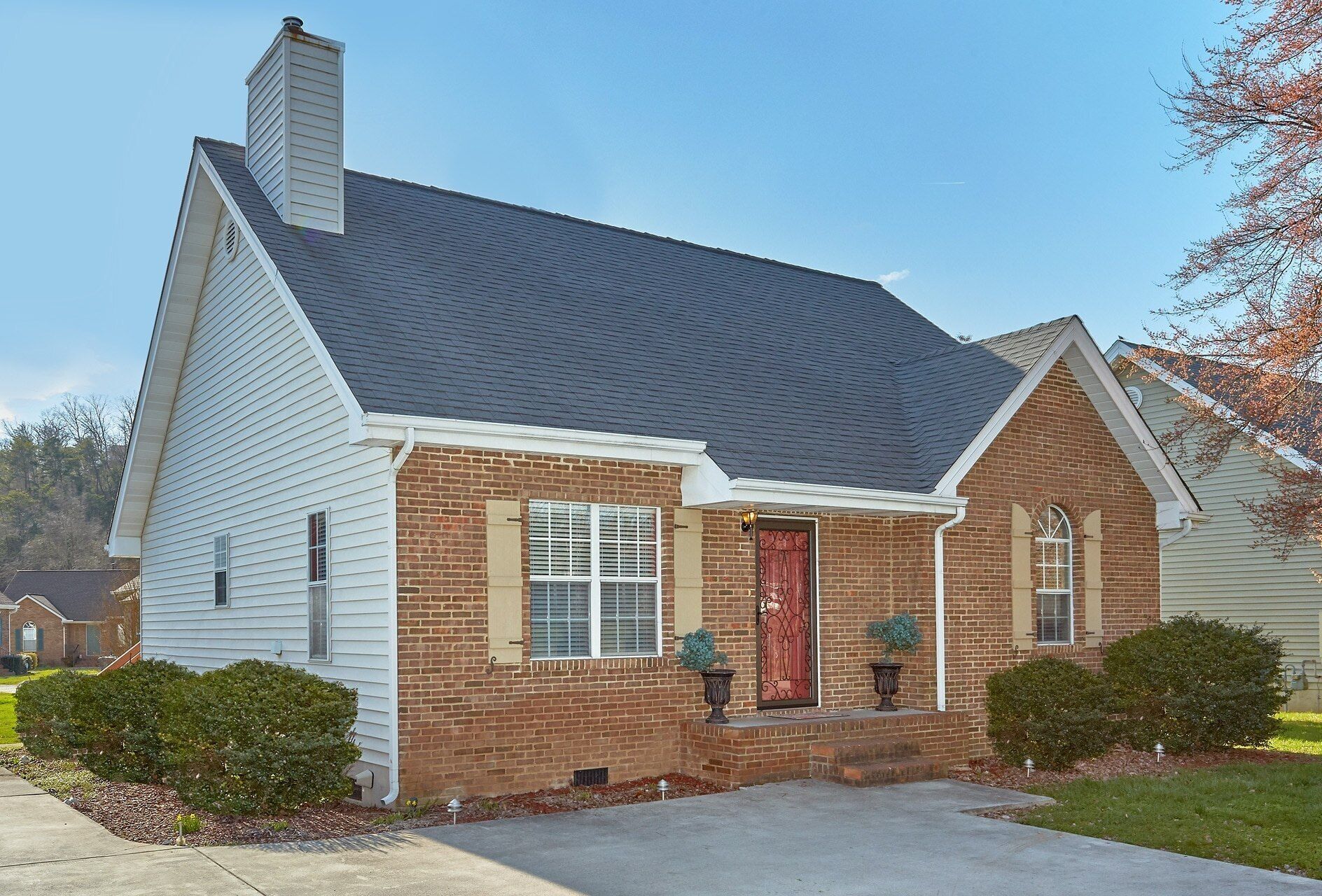 A two-story house with a brick facade, a dark shingled roof, and a front entrance with a red door.