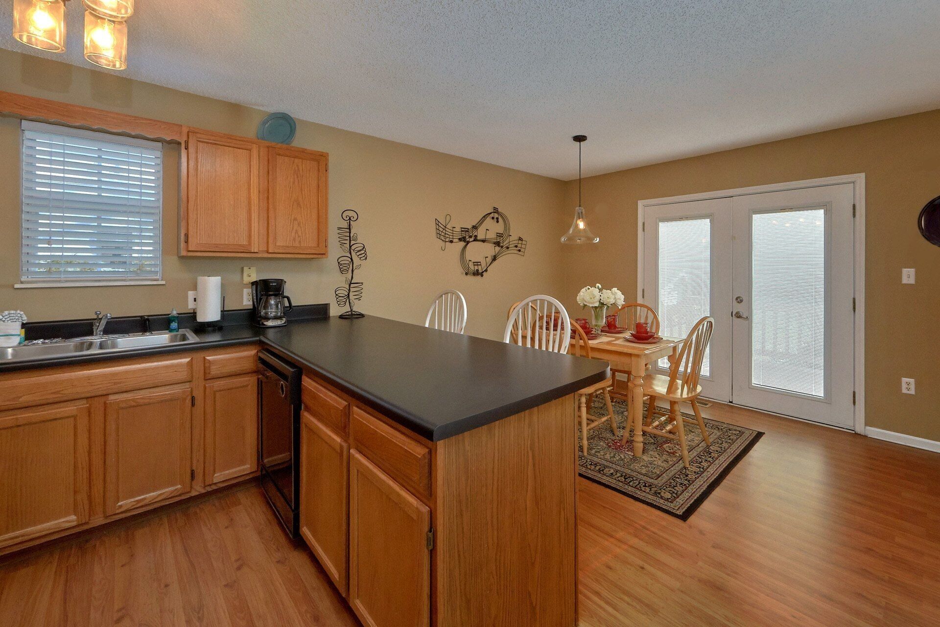A kitchen with wooden cabinets, a black countertop, a coffee maker, and a dining area with chairs and a table.