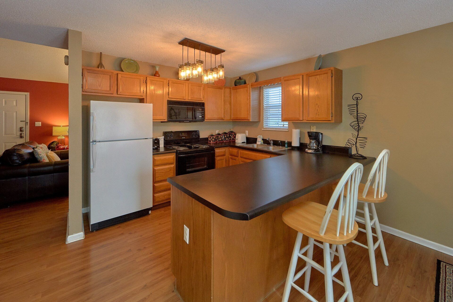 A kitchen with wooden cabinets, a central island with bar stools, a refrigerator, a stove, and a microwave.