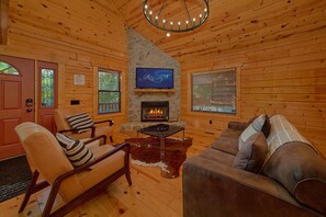 A cozy cabin interior with a fireplace, wooden walls, a television, and leather furniture.