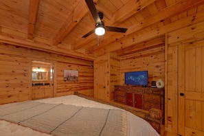 A wooden cabin interior with a bed, a ceiling fan, a television, and a cabinet.