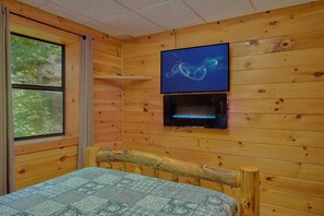 A wooden cabin room with a bed, a television mounted on the wall, and a fireplace. - One More Night | Smoky Mtn Views, Hot Tub, Near Dollywood, Game Room + Free Attraction Tickets (Pigeon Forge)