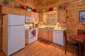 A wooden cabin-style kitchen with a refrigerator, stove, microwave, sink, and a dining area with a chair and table. - Our Happy Place | Hot Tub, Near Dollywood, Game Room, Fireplace + Free Attraction Tickets (Pigeon Forge)
